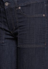 Tmavě modré džíny vyrobené z jemného denimového materiálu, s přední kapsou, kovovým knoflíkem a kontrastním stehováním podél švů.