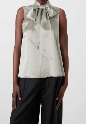 Blouse sans manches en satin gris clair avec un grand nœud à nouer au col, portée avec un pantalon noir ample, visible de la moitié du torse jusqu'aux hanches.