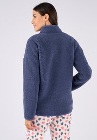 Marineblauwe fleecejas met hoge kraag, gestructureerde buitenkant, ruime pasvorm en lange mouwen. Gecombineerd met gestreepte crèmekleurige pyjamabroek.