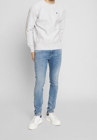 Hellgrauer Pullover mit Rundhalsausschnitt, gerippten Bündchen und Saum, kombiniert mit hellblauen Slim-Fit-Jeans und weißen Sneakers mit marineblauen Akzenten.