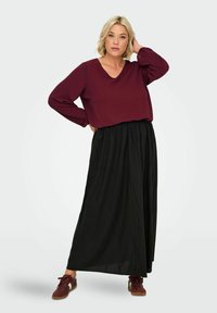 Maroon long-sleeve top with a V-neck, paired with a black, flowing maxi skirt. Model wears burgundy sneakers, showcasing a relaxed fit.