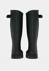 Juodos guminių kelnių ilgio botai su tekstūruota danga, sustiprinta kulno dalimi ir reguliuojamomis diržais viršuje, užtikrinančiais tvirtą prigludimą.