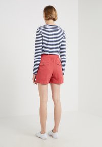 Maglietta a righe a maniche lunghe con collo rotondo abbinata a pantaloncini rossi con tasche posteriori e vita piatta, indossata con scarpe da ginnastica bianche.