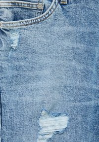 Jean en denim bleu clair avec un design usé comprenant des déchirures effilochées. Comprend un bouton argenté et des coutures contrastantes orange.