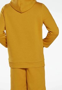 Sweat à capuche jaune en tissu doux avec une poche kangourou, des poignets et un ourlet côtelés. Doté d'une grande capuche. Assorti à un short coordonné.