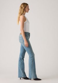 Světle modré rozšířené džíny z denimu s přiléhavým pasem, s kapsami na zadní straně a jemným logem značky na pasu.