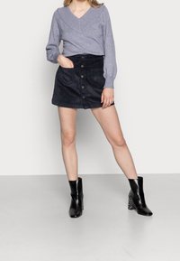 Šedý svetr s výstřihem do V a nafouklými rukávy, spojený s mini sukní z modrého manšestru s předními knoflíky a bočními kapsami, doplněný černými botami na podpatku.