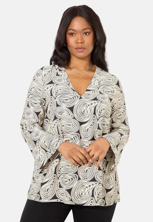 Schwarz-weiße Bluse mit floralem Muster, V-Ausschnitt und Glockenärmeln aus einem leichten Stoff. Kombiniert mit schwarzen Hosen.