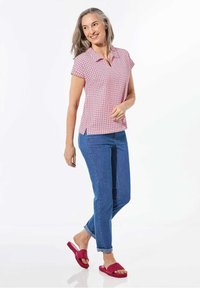 Korte mouwen polo shirt in roze en wit met patroon, voorzien van een kraag, gecombineerd met blauwe jeans en roze sandalen. Heeft zijsplitten voor meer bewegingsvrijheid.