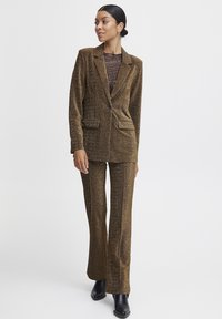 Brauner, funkensprühender Blazer und passende Hose in figurschmeichelndem Design; verfügt über zwei Vordertaschen und einen Ein-Knopf-Verschluss. Wird mit einem transparenten Oberteil kombiniert.