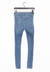 Jeans ajustados de denim azul que presentan un clásico diseño de cinco bolsillos. La tela parece ligeramente texturizada con un acabado suave.