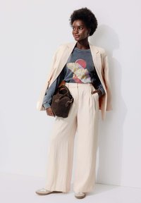 Pantalons larges crème, sweat-shirt graphique gris, blazer beige clair, sac marron et baskets beiges avec un accent blanc. Textures lisses.