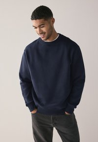 Mornarsko plavi dukserica od mekanog materijala s okruglim izrezom, rebrastim rukavima i donjim rubom; uparen s tamnosivim trapericama.