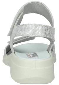 Hvide sandaler med teksturerede syntetiske remme, justerbare velcro lukninger og en polstret hvid sål, der har en let hæl og et logo på indersålen.