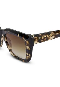 Sluneční brýle s želvovinovým vzorem, odvážným čtvercovým rámem, tmavými skly a zlatými akcenty. Název značky 'Kapten & Son' je vyrytý na straně.