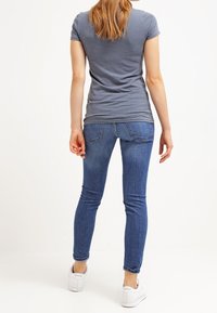 Camiseta gris de manga corta combinada con jeans ajustados de mezclilla azul y zapatillas blancas. Los jeans tienen un corte clásico y un ligero desgaste.