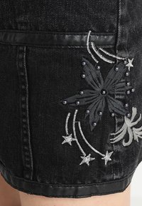 Svart denimkjol med broderad blommönster, texturerade accenter och dekorativa pärlor. Har en kontrasterande midjeband och sömmar.