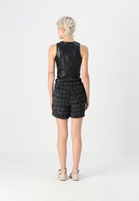 Haut sans manches en cuir noir associé à un short taille haute à motifs en damier noir et blanc. Chaussures à plateformes à lanières de couleur claire.
