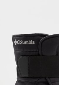 Lähikuva mustasta Columbian talvisaappaan päällisestä, jossa on pehmustettu kangas ja leveä säädettävä tarranauhavyö.