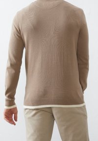 Ljusbrun stickad tröja med långa ärmar, rund halsringning och vit detalj vid fållen, kombinerad med ljusbeige byxor.