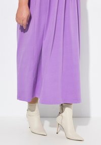 Lila, polvenpituinen mekko, joka on valmistettu sileästä kankaasta, yhdistettynä kermanvärisiin, kärjeltään teräviin nilkkabootseihin, joissa on sivuvetoketju ja tiukka muoto.