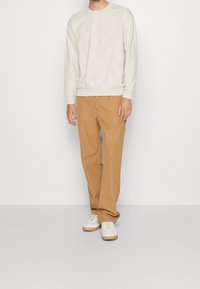 Sweat-shirt gris clair avec motif circulaire en relief, associé à un pantalon droit beige et des baskets basses blanches.