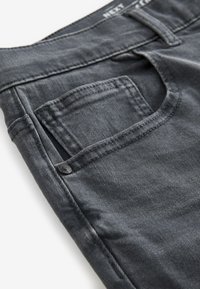 Jean en denim gris foncé en gros plan montrant la poche avant avec petite poche à pièces et détail de rivet métallique.