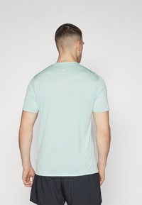 Camiseta atlética de color azul claro con cuello redondo y mangas cortas, que presenta un pequeño logo en la parte central de la espalda, fabricada con un material transpirable.