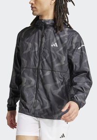 Leichte schwarze Jacke mit geometrischem Muster, Reißverschluss, Kapuze und elastischen Bündchen. Verfügt über ein Logo auf der linken Brust und Armakzentuierungen.