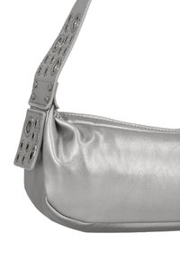 Ezüst bőr kézitáska sima textúrával, vállpánttal, amelyet kör alakú kivágások és fémes díszítések díszítenek.