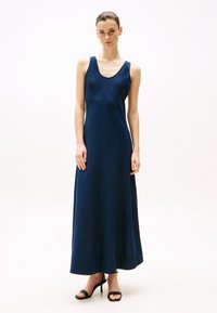 Abito maxi senza maniche di colore blu navy con scollatura a girocollo, design fluido e texture liscia. Indossato con tacchi alti neri con cinturini.