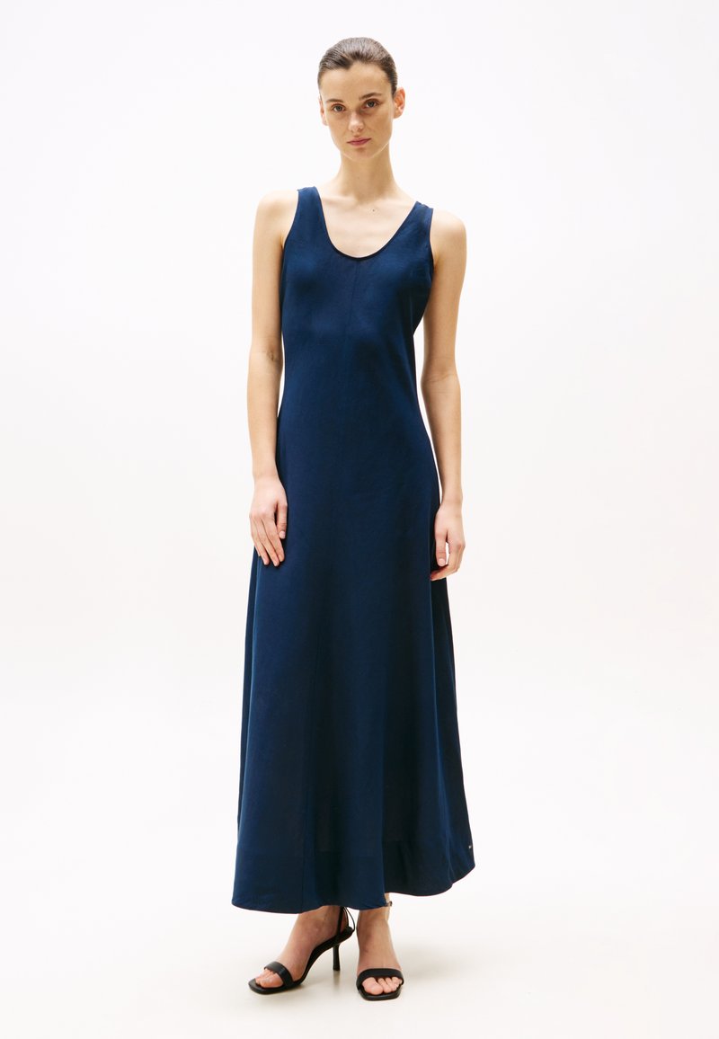Abito maxi senza maniche di colore blu navy con scollatura a girocollo, design fluido e texture liscia. Indossato con tacchi alti neri con cinturini.