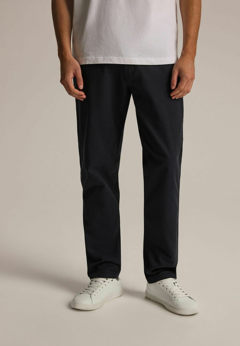 Granatowe spodnie wykonane z miękkiego materiału, o prostym kroju, z paskami na pasek i bocznymi kieszeniami, zestawione z białymi sneakersami.