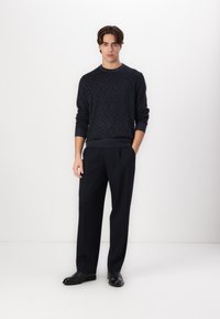 Donkerblauwe gebreide trui met ruitpatroon, gecombineerd met op maat gemaakte zwarte broek en zwarte schoenen. Het model staat tegen een witte achtergrond.