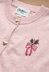 Soft pink cardigan with ribbed collar, gold heart-shaped buttons, and small embroidery of a pink bow with green leaves on the chest.