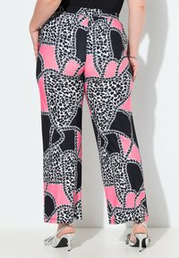 Pantaloni rosa e neri a fantasia con una vestibilità ampia, caratterizzati da accenti bianchi e dettagli arricciati, abbinati a tacchi argento.