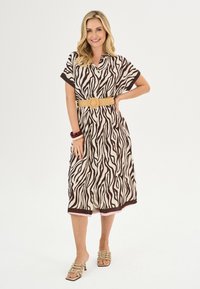 Bruin en crèmekleurig zebra-print jurkje met een kraag, korte mouwen en een stroken riem. Getextureerde stof, tot op de knie, met een roze zoom als accent.