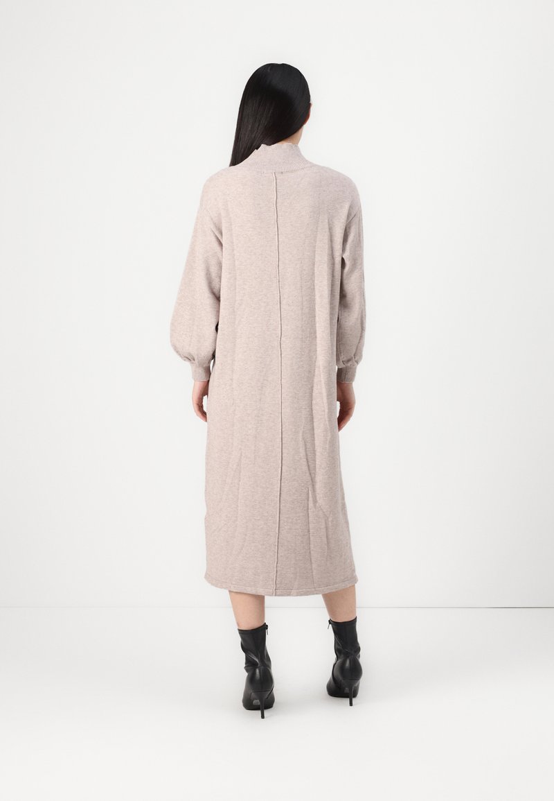 Beżowa sukienka do kolan z długimi, bufiastymi rękawami i wysokim kołnierzem. Posiada centralny szew z tyłu oraz miękką, teksturowaną tkaninę.