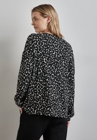 Schwarz-weißer Leopardenprint langärmliges Oberteil mit lockerer Passform, Rundhalsausschnitt und Bündchen. Weicher Stoff, sichtbare Nähte und abfallende Schultern.