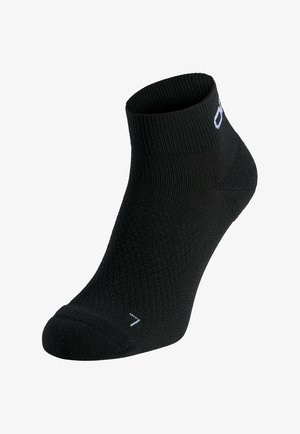 Schwarze Knöchelsocke mit geripptem Bündchen und strukturiertem Strickmuster, mit einem kleinen weißen Logo nahe der Oberseite und einem weißen Buchstaben "L" auf der Zehenpartie.