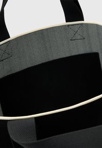 Tote taske med sort tekstil yderside, gråt indre med kontrasterende cremefarvet kant, flere lommer og robuste sorte håndtag.