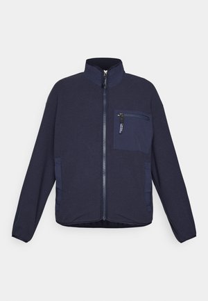 Chaqueta de forro polar azul marino con cremallera frontal completa, bolsillo en el pecho con cremallera, dos bolsillos laterales y cuello alto.