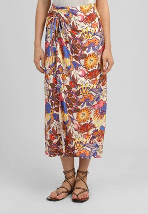 Jupe midi colorée avec des motifs célestes et floraux, portée avec des sandales plates marron à brides sur un fond gris clair.