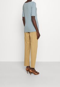 Ljusblåt figursydd topp med trekvartslånga ärmar, parat med beige byxor och bruna högklackade sandaler. Enkelt design och slät textur.