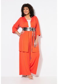Completo brillante arancione in due pezzi, con un top in stile kimono a maniche larghe e un pantalone largo coordinato, stretto in vita con una cintura metallica.