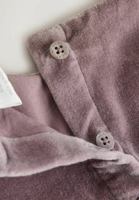 Samtstoff in sanftem Mauve, mit einem umgeschlagenen Kragen und zwei Knöpfen mit eingeprägtem "NEXT". Glatte Textur mit geringfügigem Flaum.