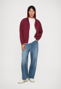 Sweat-shirt à capuche bordeaux, t-shirt blanc à col rond, jeans droits bleu clair et baskets blanches. Tenue décontractée avec des textiles superposés.
