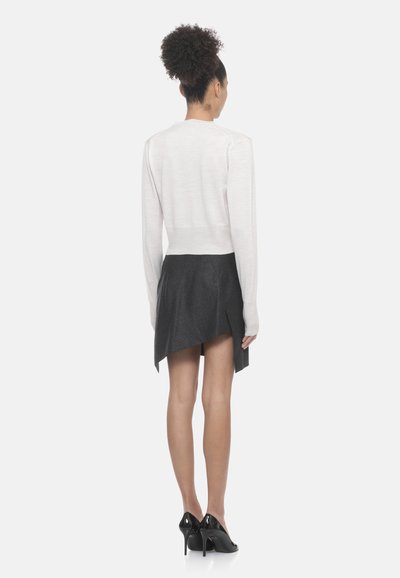 Maglione grigio chiaro accorciato abbinato a una gonna grigia scura a vita alta, con orlo asimmetrico e tacchi neri eleganti.