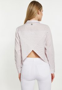 Camicia a maniche lunghe a righe in colori pastello con design a schiena scoperta. Presenta un bottone al collo e una forma rilassata. Abbinata a jeans bianchi.