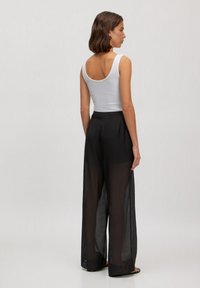 Weißes Tanktop, schwarze durchsichtige weite Hose, einfaches Design, glatte Textur, gesäumte Kanten, knöchellang, mit lockerer Passform.